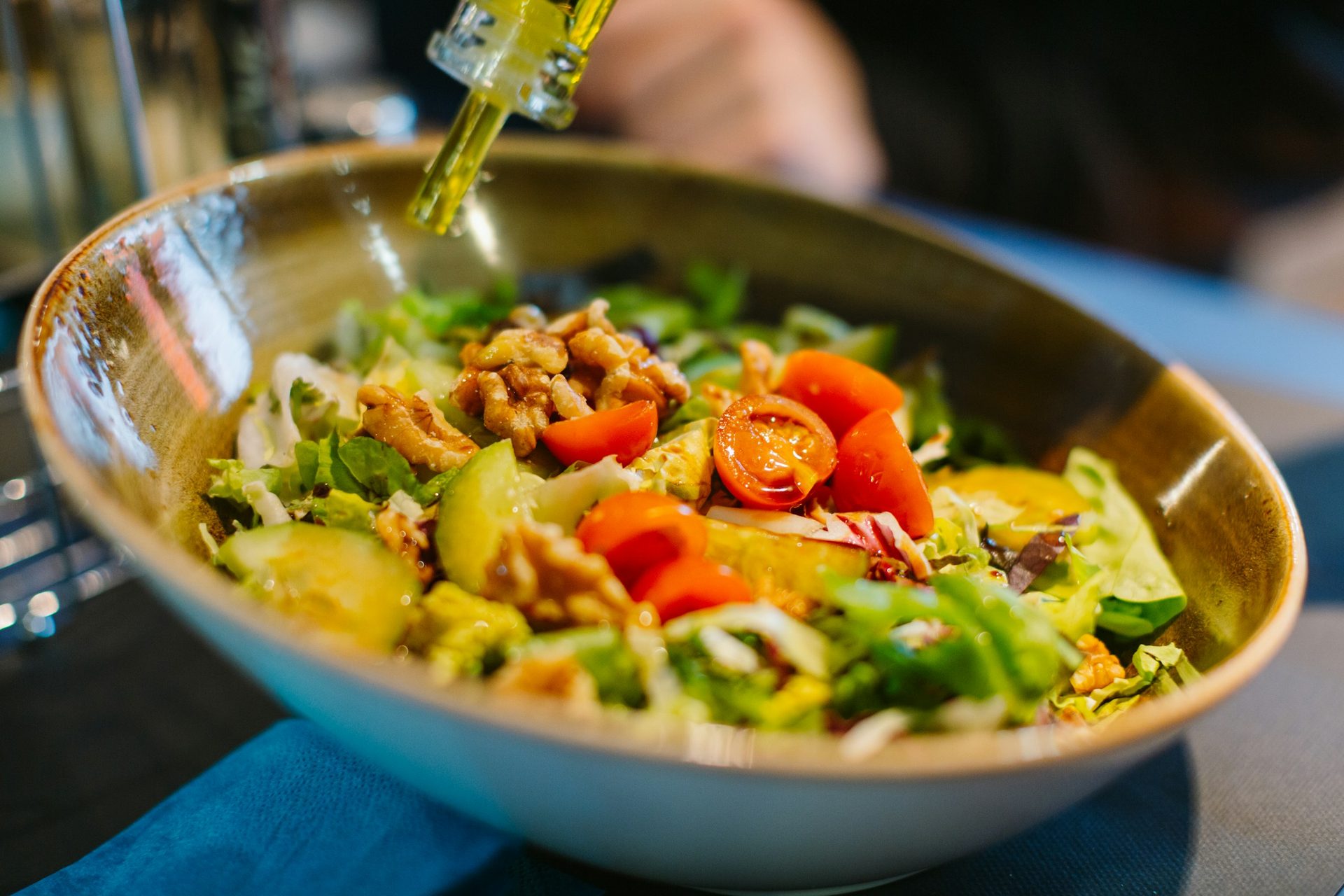 Salat mit Tomaten, Gurke und Walnüssen in einer Schale, darüber wird Öl geträufelt