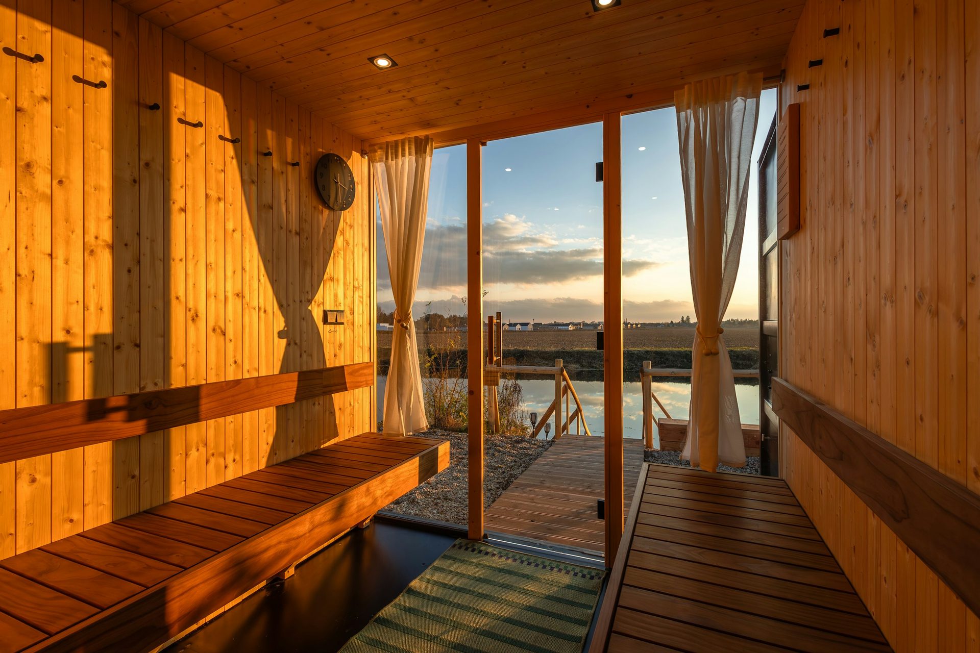 Wooden sauna with an open door onto a jetty and a lake at sunset