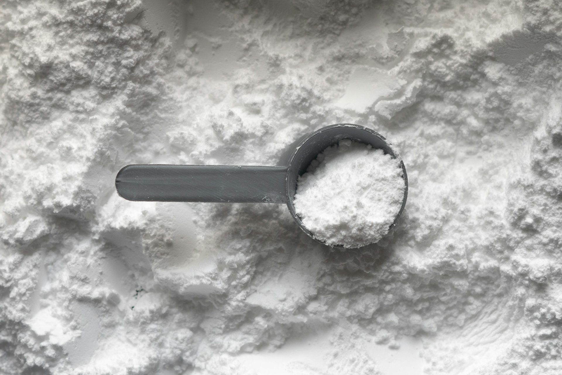 Grauer Messlöffel mit weißem Kreatinpulver auf einem Haufen Pulver