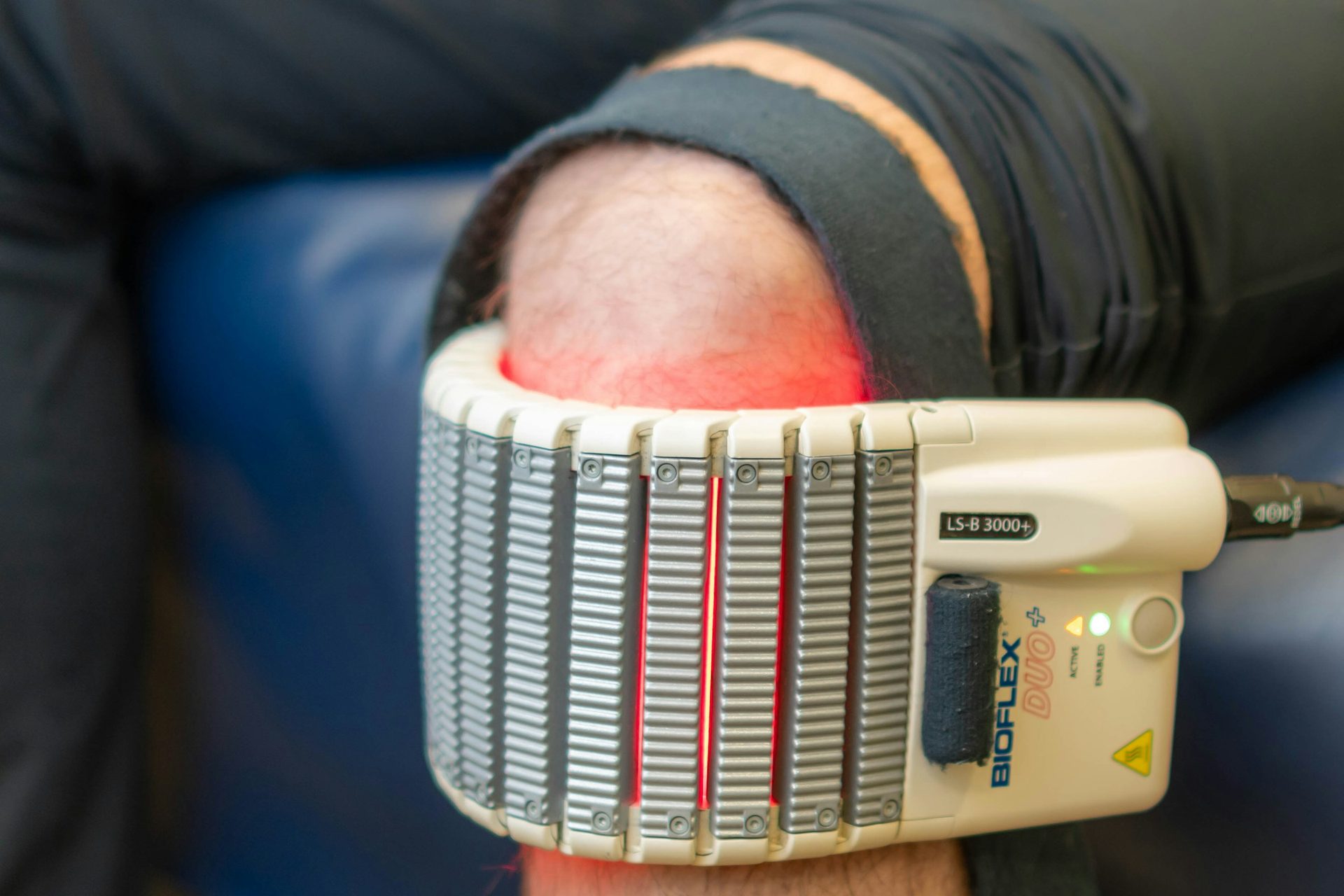 Gerät für Rotlichttherapie um ein Knie geschnallt, das rot auf der Haut leuchtet