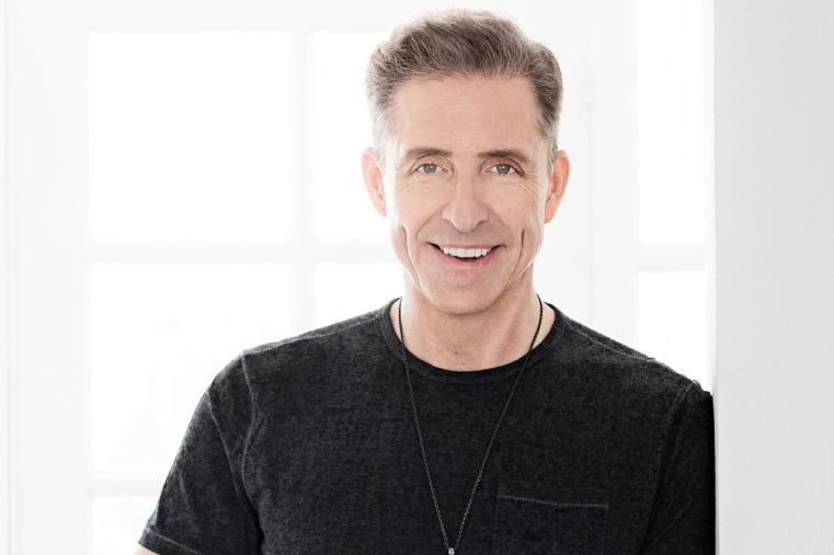 Dave Asprey smiling in a black T-shirt in front of a bright window