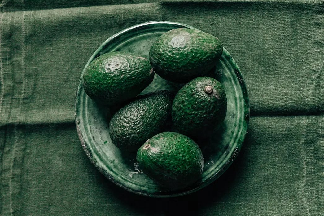 Avocados in a green ceramic bowl on a green linen cloth